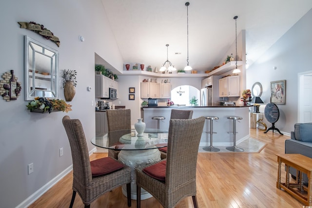 dining room featuring a chandelier, high vaulted ceiling, and light hardwood / wood-style flooring