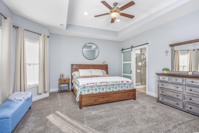 bedroom featuring ensuite bathroom, a tray ceiling, light colored carpet, ceiling fan, and a barn door