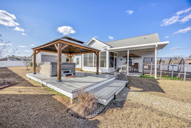 rear view of property with a gazebo, a sunroom, a deck, and a hot tub