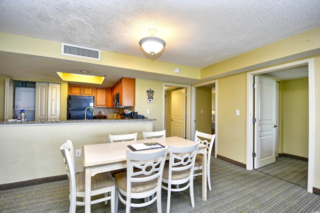 dining space featuring carpet flooring, sink, stacked washing maching and dryer, and a textured ceiling