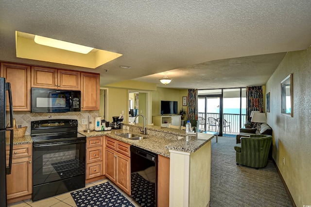 kitchen with black appliances, expansive windows, sink, light stone counters, and kitchen peninsula