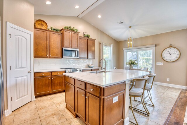 kitchen with backsplash, vaulted ceiling, sink, decorative light fixtures, and an island with sink