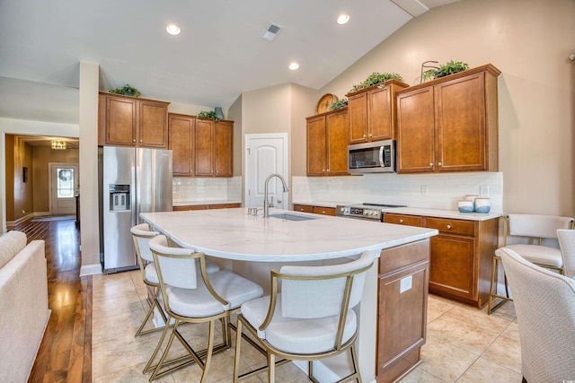 kitchen featuring sink, a kitchen breakfast bar, an island with sink, lofted ceiling, and appliances with stainless steel finishes