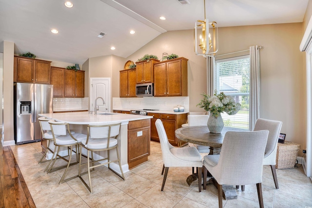 kitchen with sink, hanging light fixtures, lofted ceiling, a center island with sink, and appliances with stainless steel finishes