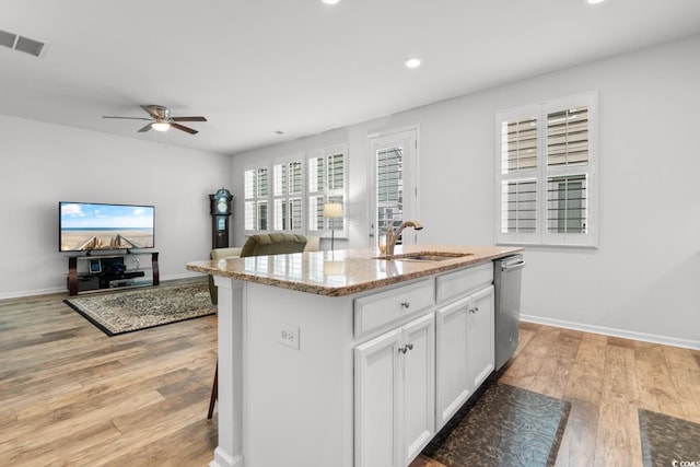 kitchen featuring light stone countertops, white cabinetry, sink, stainless steel dishwasher, and an island with sink