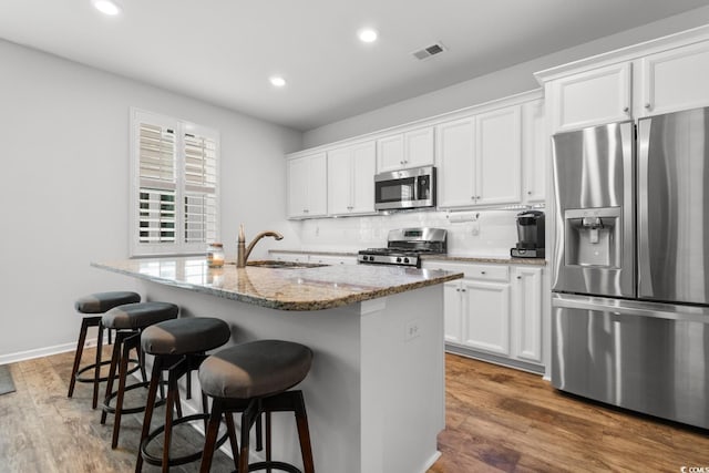 kitchen featuring white cabinetry, stainless steel appliances, light stone counters, dark hardwood / wood-style flooring, and an island with sink