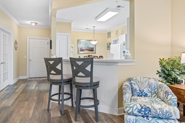 kitchen with hanging light fixtures, kitchen peninsula, white fridge, a breakfast bar, and ornamental molding