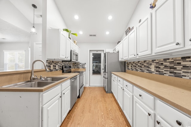 kitchen with white cabinets, sink, vaulted ceiling, appliances with stainless steel finishes, and decorative light fixtures