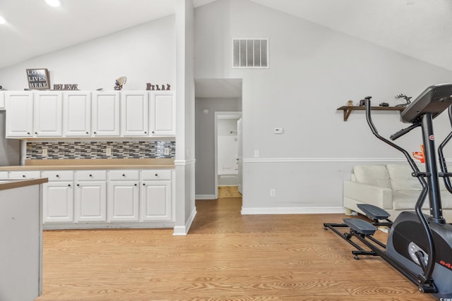 kitchen with white cabinets, decorative backsplash, light wood-type flooring, and vaulted ceiling