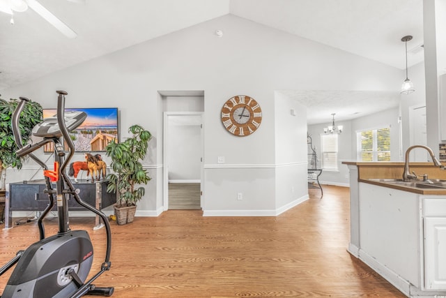 workout area featuring ceiling fan with notable chandelier, vaulted ceiling, sink, and light hardwood / wood-style flooring