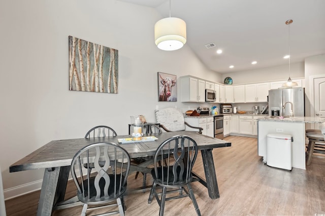 dining area featuring light wood-type flooring, visible vents, lofted ceiling, and baseboards