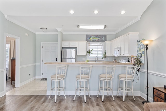 kitchen with a kitchen breakfast bar, kitchen peninsula, stainless steel fridge, and white cabinetry