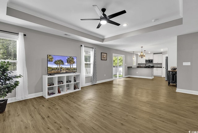 unfurnished living room featuring a tray ceiling, dark hardwood / wood-style flooring, and ceiling fan with notable chandelier