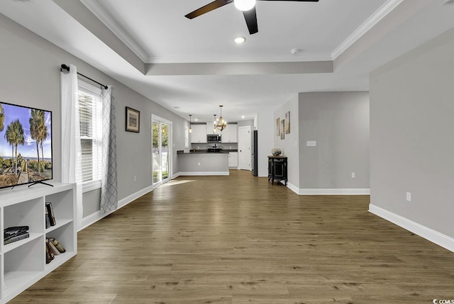 unfurnished living room featuring hardwood / wood-style floors, ceiling fan with notable chandelier, a raised ceiling, and crown molding