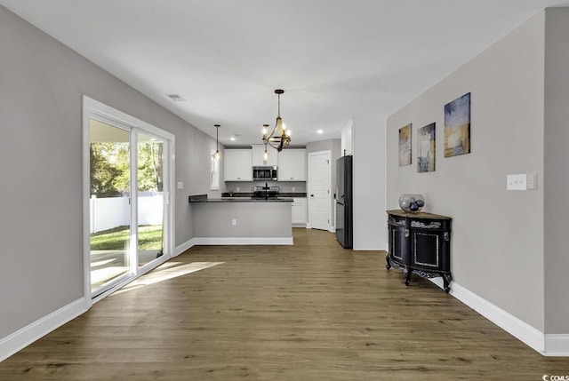 kitchen with dark wood-type flooring, a notable chandelier, pendant lighting, white cabinets, and appliances with stainless steel finishes