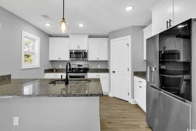 kitchen featuring sink, dark stone countertops, white cabinetry, wood-type flooring, and stainless steel appliances