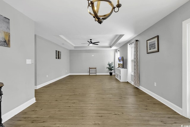 unfurnished living room with hardwood / wood-style floors, ceiling fan with notable chandelier, and a raised ceiling