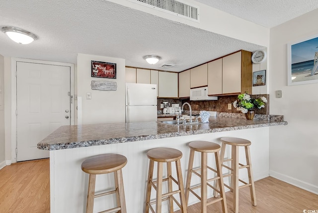 kitchen with decorative backsplash, kitchen peninsula, a textured ceiling, white appliances, and light hardwood / wood-style flooring