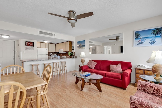 living room featuring ceiling fan, light hardwood / wood-style flooring, and a textured ceiling