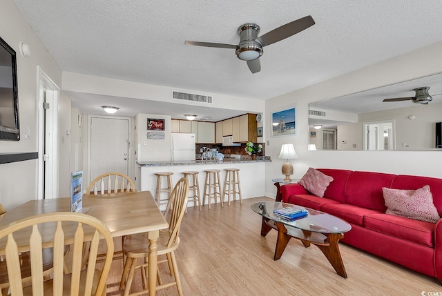 living room with a textured ceiling, light hardwood / wood-style flooring, and ceiling fan