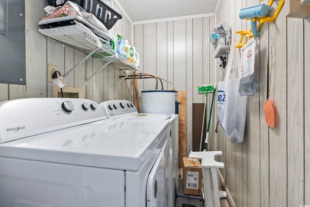 laundry room featuring water heater, washer and clothes dryer, a textured ceiling, and wooden walls