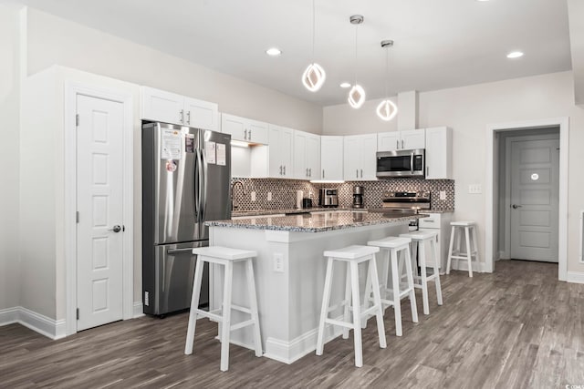 kitchen featuring dark stone counters, appliances with stainless steel finishes, decorative light fixtures, white cabinetry, and a breakfast bar area