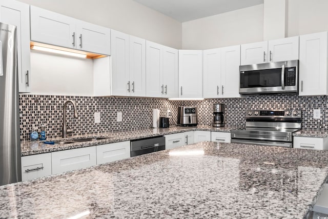 kitchen with light stone countertops, tasteful backsplash, stainless steel appliances, sink, and white cabinetry