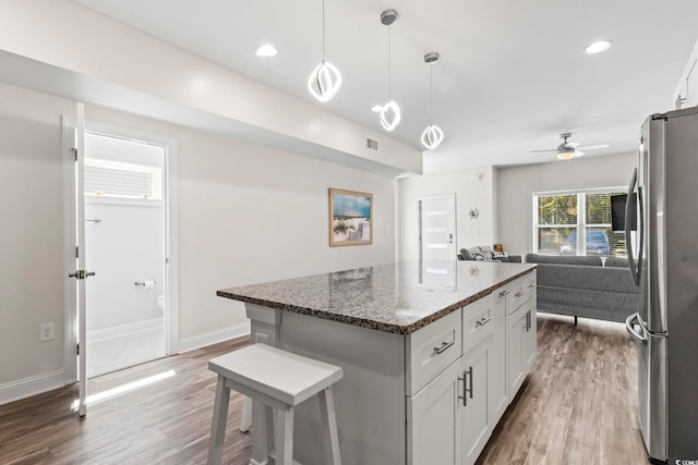 kitchen with white cabinetry, a center island, dark stone countertops, stainless steel fridge, and a breakfast bar