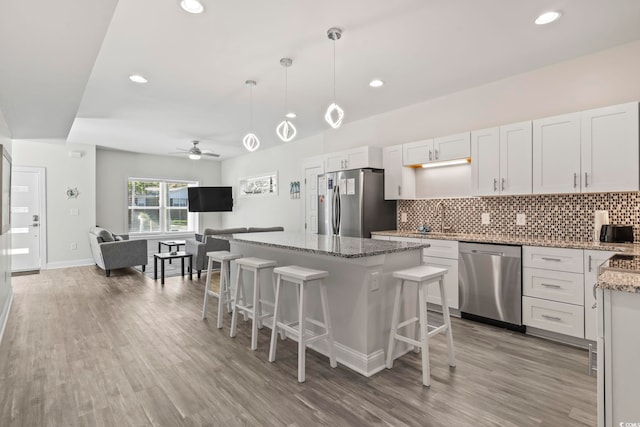 kitchen with stainless steel appliances, ceiling fan, decorative light fixtures, white cabinets, and a center island