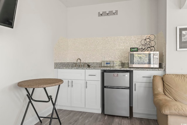 kitchen featuring backsplash, light stone counters, dark hardwood / wood-style floors, white cabinetry, and fridge