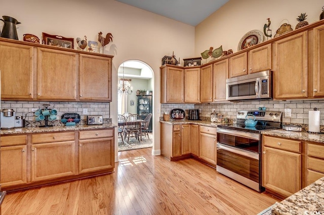 kitchen featuring light stone countertops, decorative backsplash, stainless steel appliances, a chandelier, and light hardwood / wood-style floors