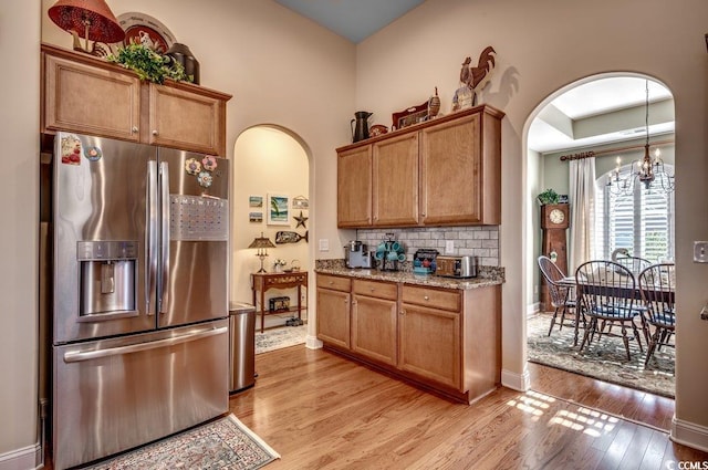 kitchen with a notable chandelier, stainless steel fridge, light stone counters, and light hardwood / wood-style flooring