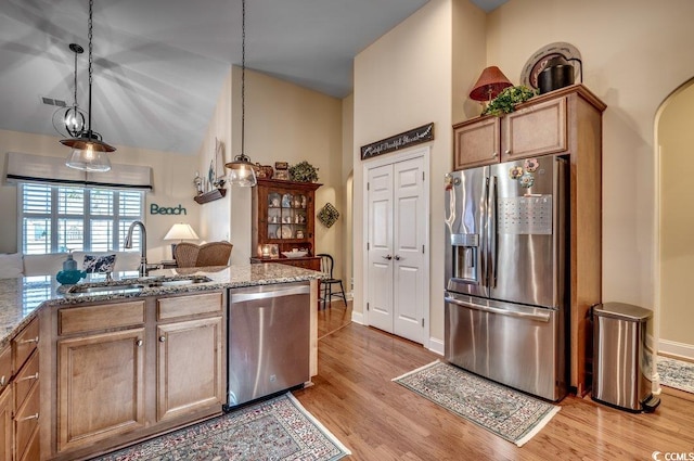 kitchen featuring pendant lighting, stone counters, sink, appliances with stainless steel finishes, and light hardwood / wood-style floors