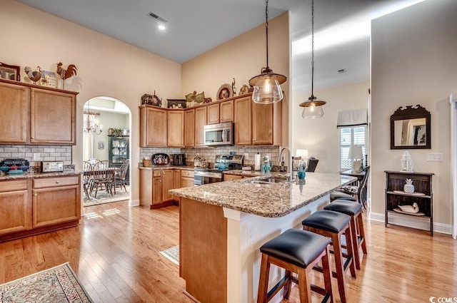 kitchen with light stone countertops, sink, hanging light fixtures, kitchen peninsula, and appliances with stainless steel finishes