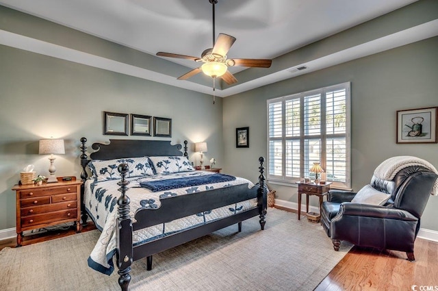 bedroom with a raised ceiling, ceiling fan, and light wood-type flooring