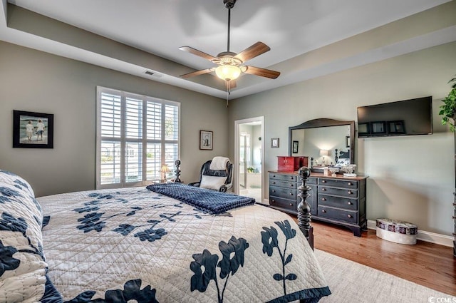 bedroom featuring light wood-type flooring, connected bathroom, a tray ceiling, and ceiling fan