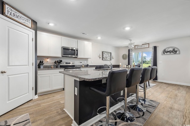 kitchen featuring light stone countertops, a kitchen breakfast bar, a kitchen island with sink, white cabinets, and appliances with stainless steel finishes