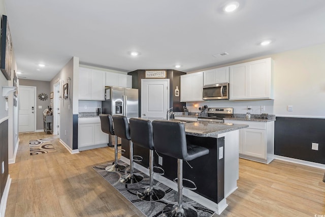 kitchen featuring a kitchen bar, white cabinetry, an island with sink, and appliances with stainless steel finishes