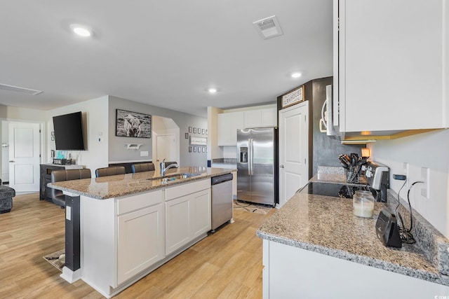 kitchen featuring white cabinets, appliances with stainless steel finishes, a breakfast bar, and a center island with sink