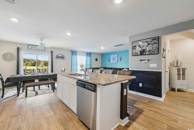 kitchen with sink, stainless steel dishwasher, an island with sink, white cabinetry, and a breakfast bar area