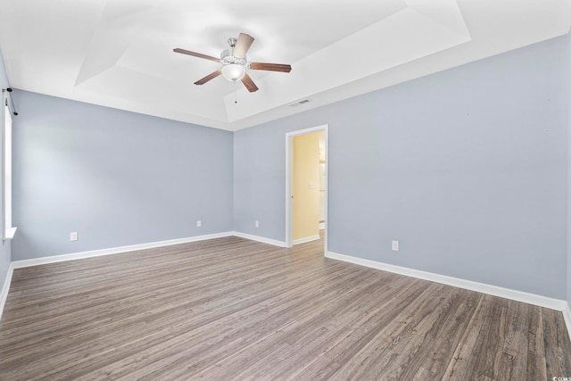 spare room with a raised ceiling, ceiling fan, and light hardwood / wood-style flooring