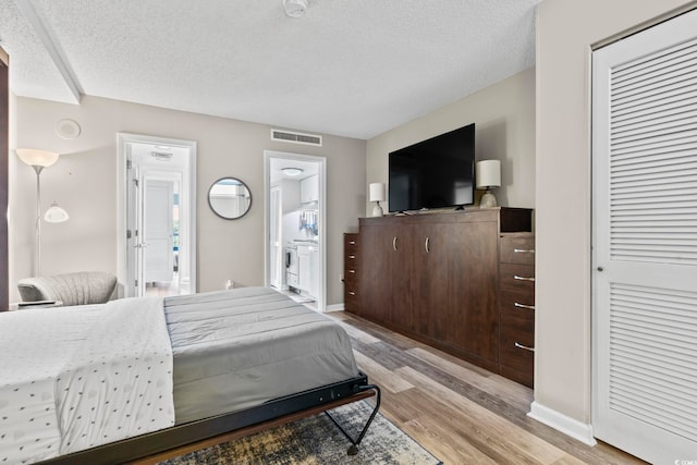 bedroom with ensuite bath, a closet, light hardwood / wood-style floors, and a textured ceiling