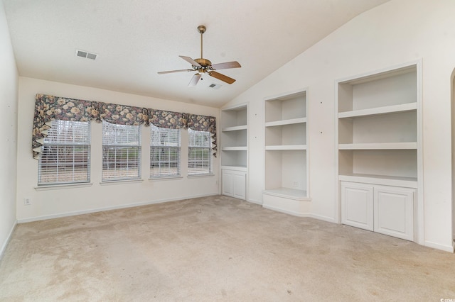 unfurnished living room featuring lofted ceiling, light carpet, ceiling fan, built in features, and a textured ceiling