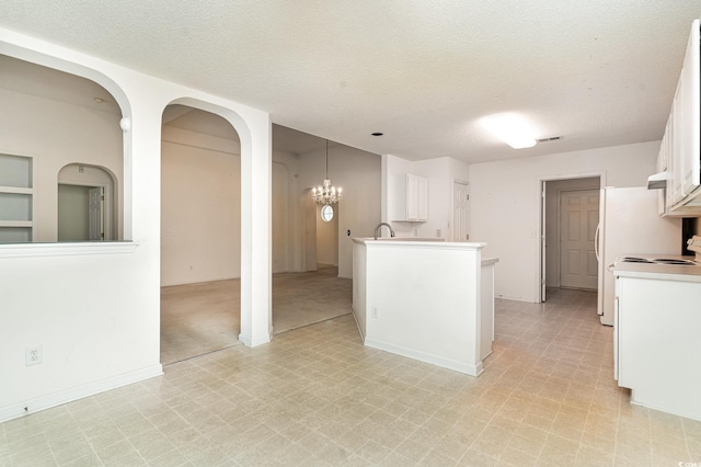 kitchen with kitchen peninsula, a textured ceiling, decorative light fixtures, white cabinets, and a chandelier