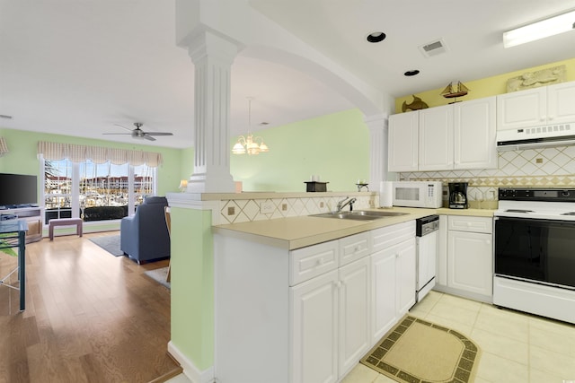 kitchen featuring kitchen peninsula, white appliances, sink, pendant lighting, and range hood