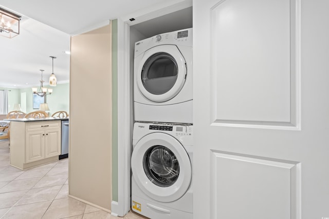 clothes washing area featuring light tile patterned floors, stacked washing maching and dryer, and a notable chandelier