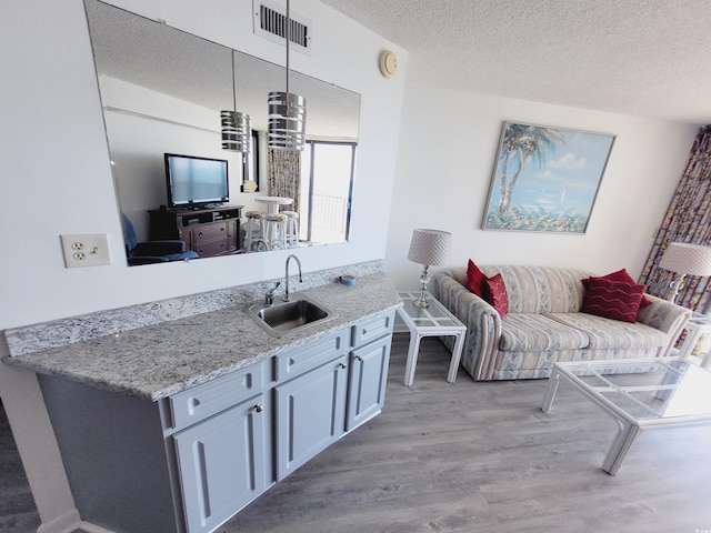 4719 S Ocean Blvd Unit 609, North Myrtle Beach, SC 29582 - kitchen featuring a sink, light wood finished floors, a textured ceiling, open floor plan, and light stone counters