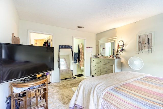 carpeted bedroom featuring a walk in closet, a closet, ensuite bath, and a textured ceiling