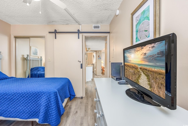 bedroom featuring ceiling fan, a barn door, a textured ceiling, light hardwood / wood-style floors, and a closet