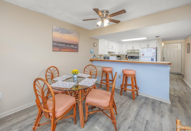 dining space with a textured ceiling, light wood-type flooring, and ceiling fan